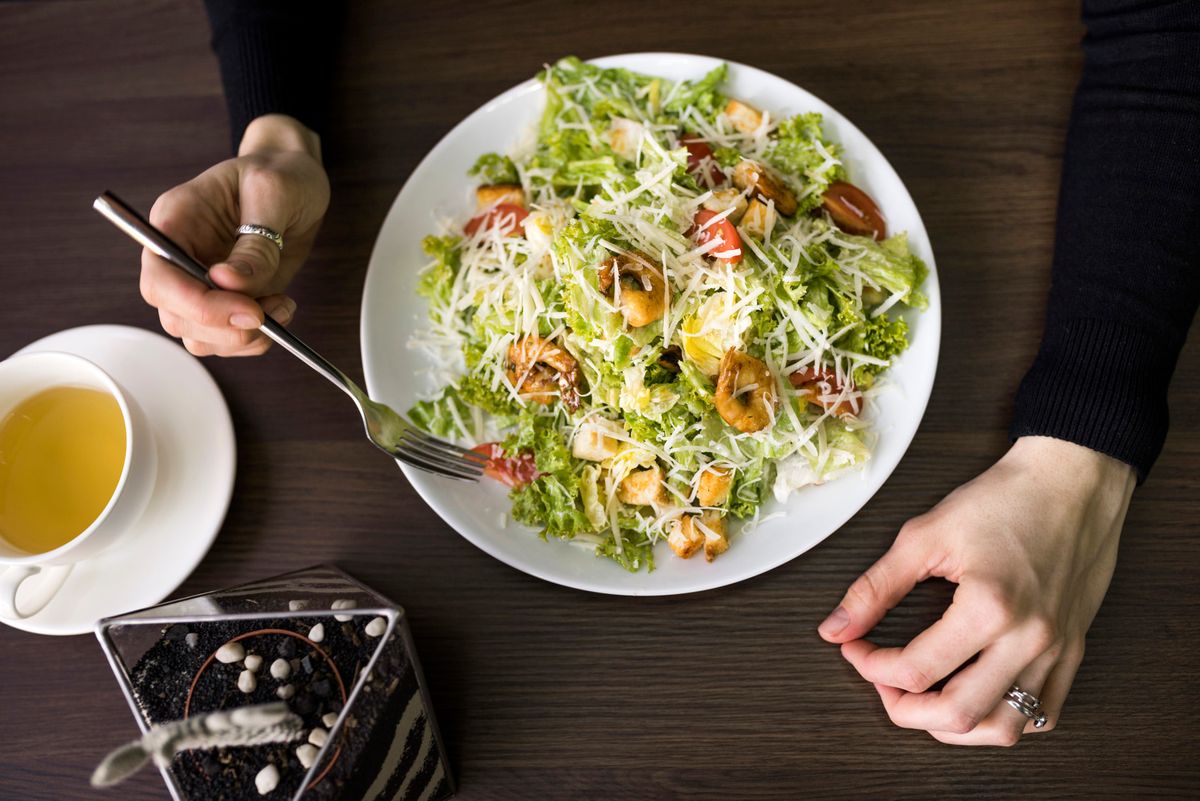 elevated-view-person-having-caesar-salad-with-shrimp-white-plate-table