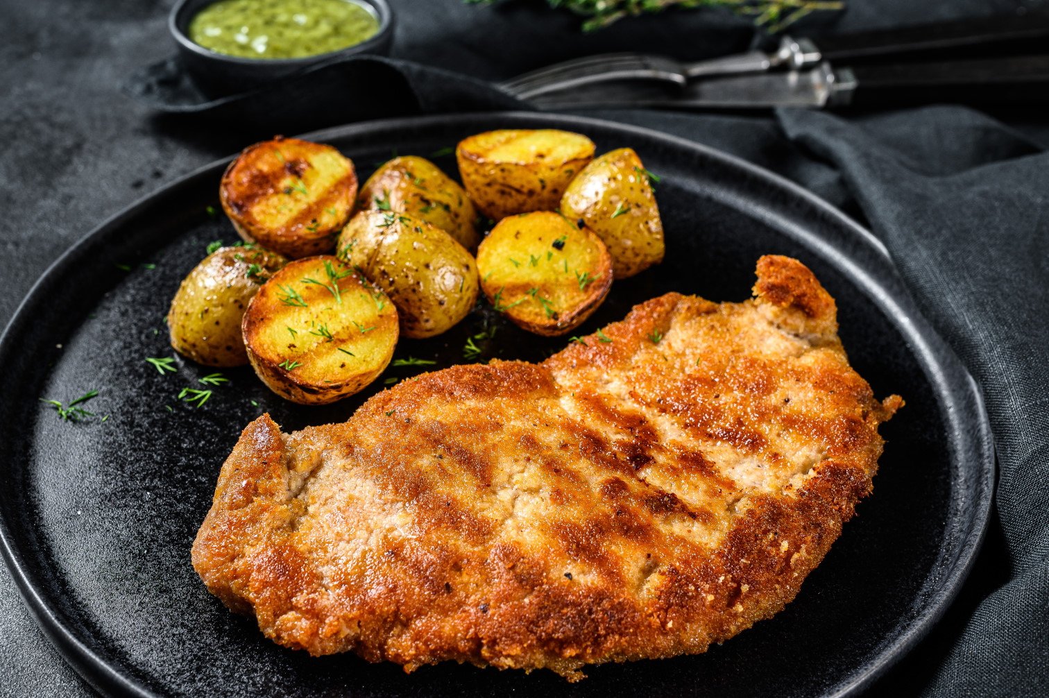 fried-chicken-schnitzel-with-baked-potatoes-black-surface-top-view